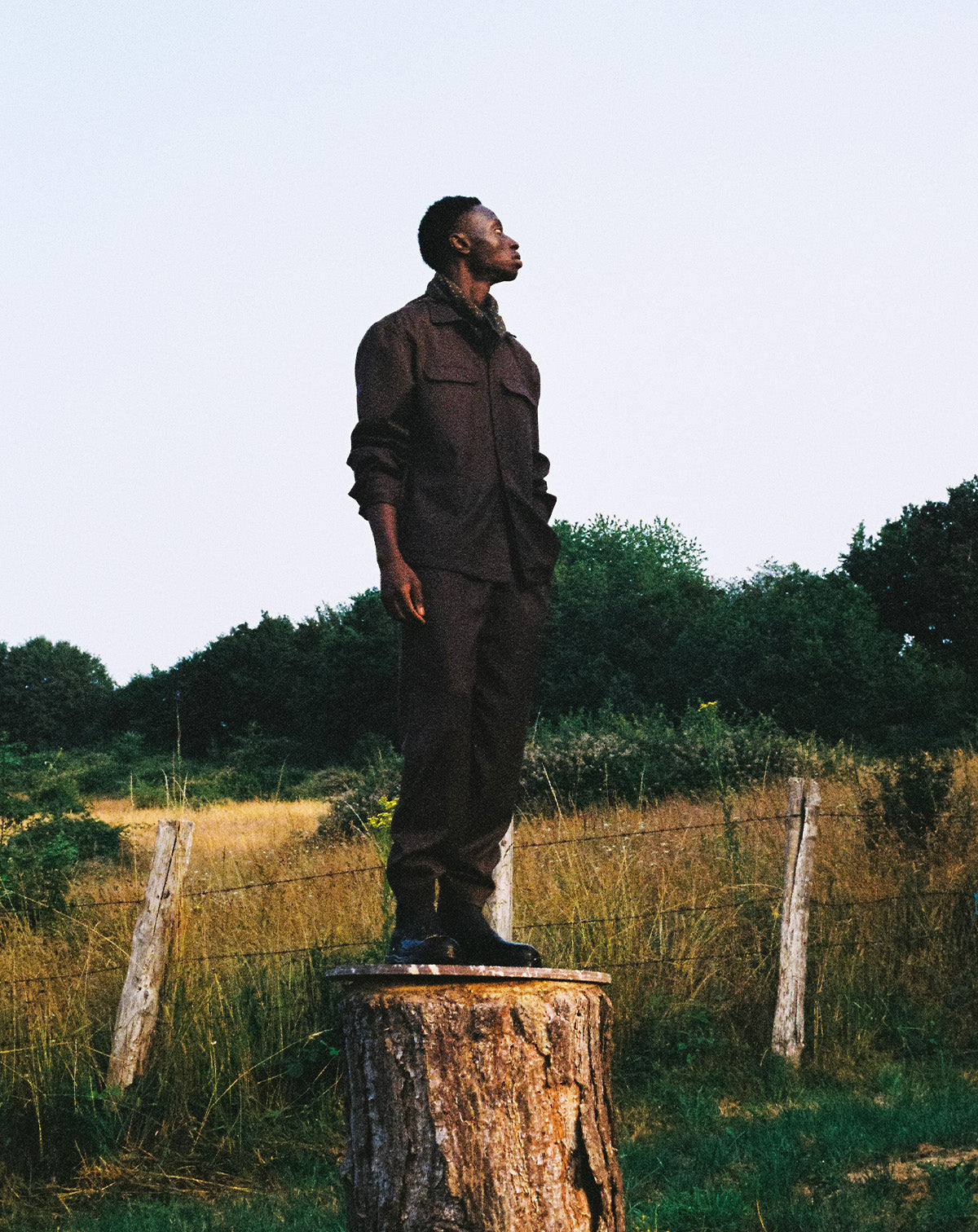homme en ensemble marron debout sur un tronc d'arbre dans un champs