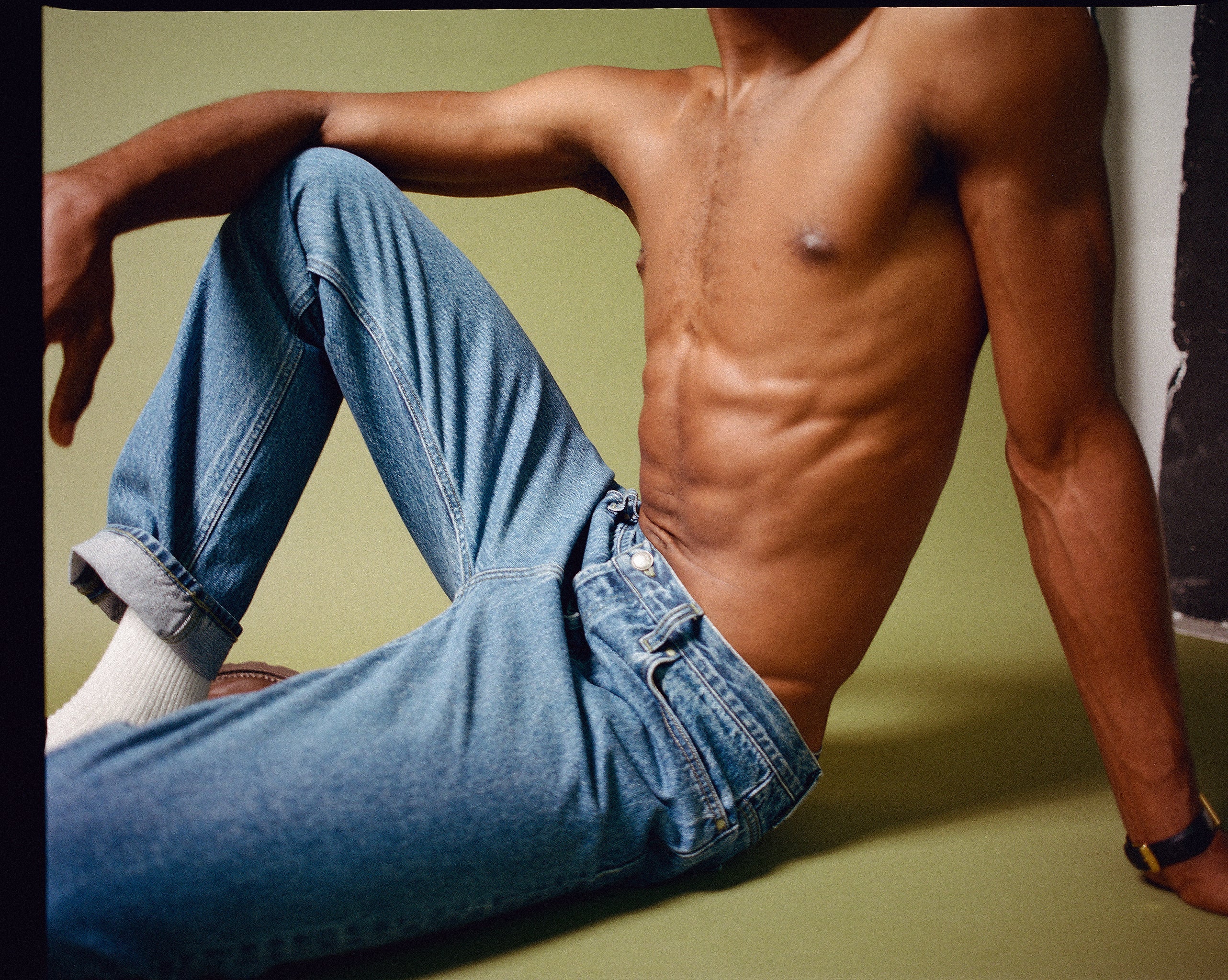 homme torse nu portant un jean bleu légèrement délavé et allongé sur un fond vert