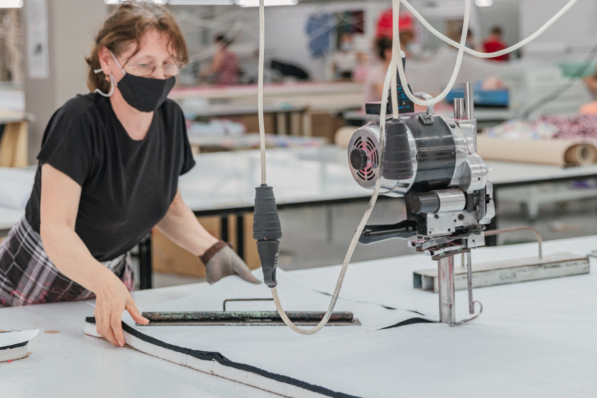Une coupeuse guide une machine de coupe sur plusieurs épaisseurs de tissu.